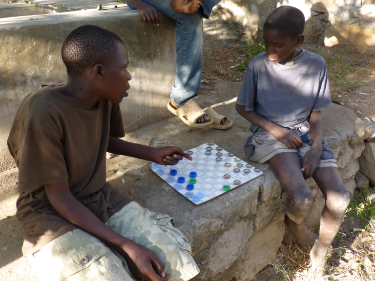 In their free time, the boys love to play games. They made this checkers board themselves from an old piece of cardboard and bottle caps.